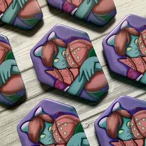 May include: Set of six purple and pink enamel pins featuring a cartoon character with green skin and pink hair hugging a robot with a green and pink helmet. The pins are shaped like a hexagon.