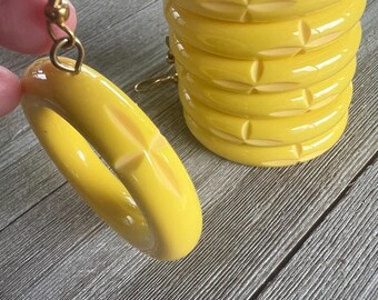 May include: Vibrant yellow hoop earrings with a carved geometric pattern. The earrings are shown with a stack of matching yellow rings. The earrings have gold-coloured hooks.