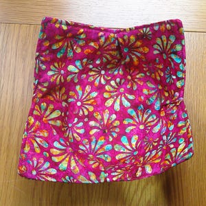 May include: A square fabric bowl cosy with a vibrant floral pattern. The cosy features a deep pink background with a repeating design of stylized flowers in shades of yellow, orange, and teal. The edges are neatly finished.