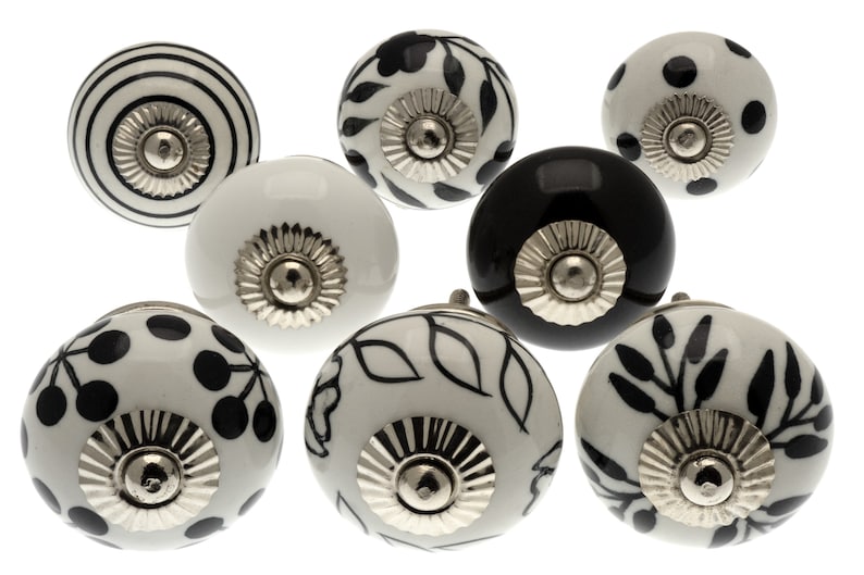 May include: Set of eight ceramic cabinet knobs with black and white patterns. The knobs have a silver finish and are round in shape.