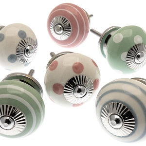 May include: Six ceramic cabinet knobs with different patterns. The knobs are white with green, pink, and blue accents. Each knob has a silver metal base.