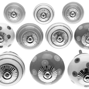 Op de afbeelding: Een verzameling decoratieve keramische kastknoppen in verschillende ontwerpen. De knoppen hebben patronen zoals strepen en stippen in grijstinten, wit en zilver. Elke knop heeft een metalen basis voor bevestiging.