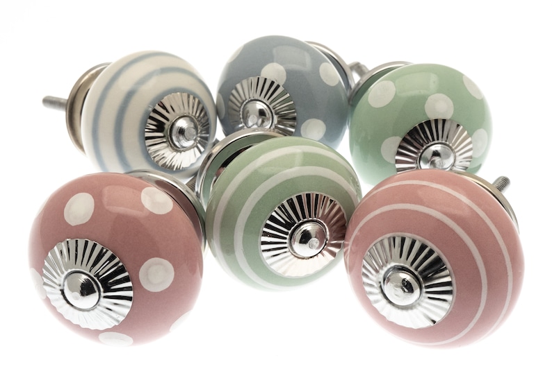 May include: Six decorative cabinet knobs in pastel shades. The knobs have stripe and polka dot patterns, with a silver-coloured base. Colours include pink, blue, green, and white. These knobs are ideal for furniture.