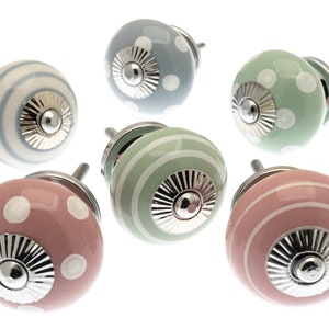 May include: Six ceramic cabinet knobs in pastel shades of pink, blue, and green. Each knob has a silver base and is decorated with either polka dots or stripes. These knobs are perfect for adding a touch of charm to furniture, and are measured in centimetres.