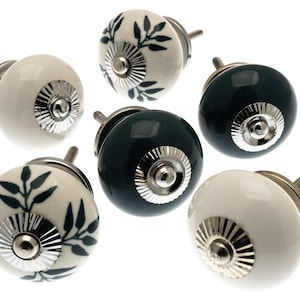 May include: A selection of seven ceramic cabinet knobs. The knobs are round with a glossy finish, in white and dark teal. Some knobs feature a silver-coloured metal base and a leaf design. The knobs are for furniture.