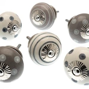 May include: Six decorative cabinet knobs in various designs. The knobs feature a round shape with a silver metal base. Some knobs are white with blue polka dots, others are gray with white polka dots, and some have gray stripes.