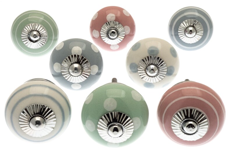 Puede incluir: Conjunto de ocho pomos de armario de cer&aacute;mica con una variedad de colores pastel y patrones, incluyendo lunares, rayas y una combinaci&oacute;n de ambos. Cada pomo tiene una base de metal plateado.
