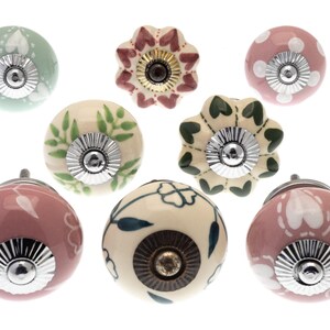 Op de afbeelding: Negen keramische kastknoppen met verschillende bloemen- en hartmotieven. De knoppen zijn in de kleuren roze, groen en cr&egrave;me met zilveren accenten.