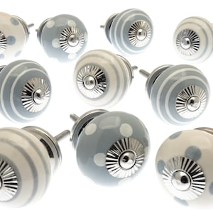 May include: A collection of ceramic cabinet knobs in various designs. Some knobs are white with blue polka dots, others are gray with white stripes, and some are white with gray stripes. Each knob has a silver metal base.
