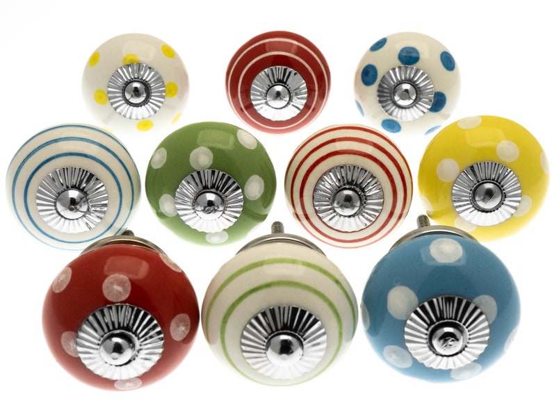 May include: Ten decorative ceramic cabinet knobs in various colours. Each knob has a round shape with a silver metal base. The knobs are painted in red, yellow, green, and blue, with polka dots and striped patterns. Ideal for furniture.