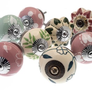 Op de afbeelding: Assortiment van keramische kastknoppen met verschillende bloemen- en bladpatronen in tinten roze, groen en wit. De knoppen hebben zilveren en gouden accenten.