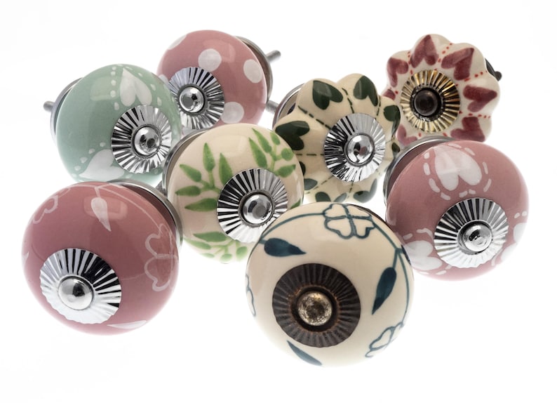Op de afbeelding: Assortiment van keramische kastknoppen met verschillende bloemen- en bladpatronen in tinten roze, groen en wit. De knoppen hebben zilveren en gouden accenten.