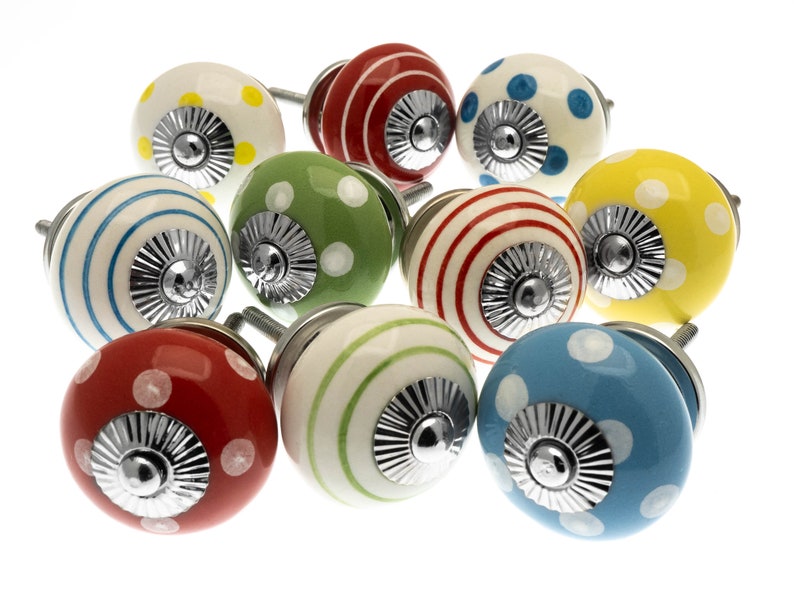 May include: A selection of decorative ceramic cabinet knobs. The knobs are spherical and feature patterns like polka dots and stripes in shades of red, yellow, green, blue, and white. Each knob has a silver metal base and screw.