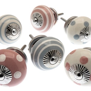 Peut inclure: Six boutons de porte en céramique avec différents motifs. Les boutons sont blancs avec des rayures roses et bleues et des pois. Les boutons ont une base en métal argenté.
