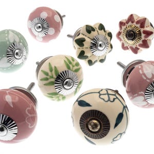 May include: Assortment of eight ceramic cabinet knobs with floral and leaf designs. The knobs are in shades of pink, green, and cream with silver accents.