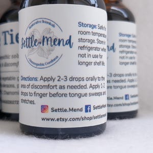May include: Close-up of several small, dark glass bottles with white labels. The labels feature the text "Settle Mend" and detailed instructions. The bottles are for homeopathic remedies, with a focus on natural ingredients.