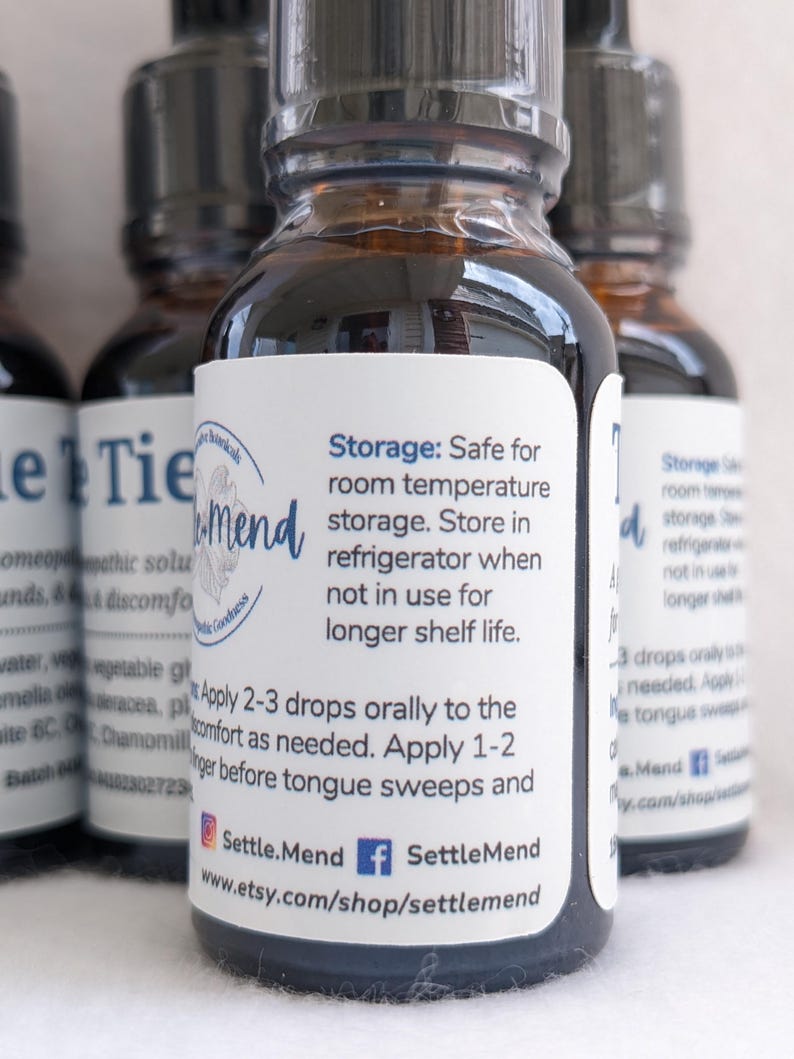 May include: Several small, brown glass bottles with black caps are arranged in a close-up shot. Each bottle has a white label with blue text, including instructions and the brand name "Settle.Mend". The bottles contain a liquid.