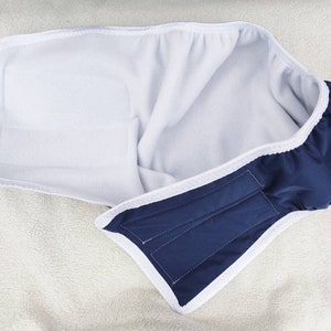 Op de afbeelding: Een blauwe en witte herbruikbare doekluier met een witte fleece voering. De luier heeft een klittenbandsluiting.