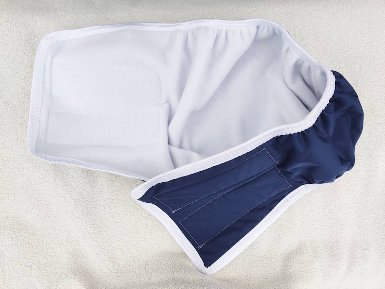 Op de afbeelding: Een blauwe en witte herbruikbare doekluier met een witte fleece voering. De luier heeft een klittenbandsluiting.