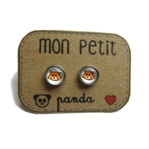 Puede incluir: Pendientes de botón plateados con diseño de panda rojo. Se exhiben en una tarjeta marrón con el texto "mon petit panda", una ilustración de panda y un corazón rojo.