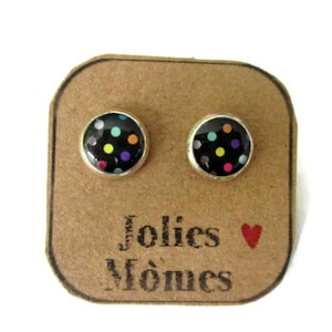 Puede incluir: Un par de pendientes de botón de plata con fondos negros y lunares de colores. Los pendientes se muestran en una tarjeta marrón con el texto "Jolies Momes" y un corazón rojo.