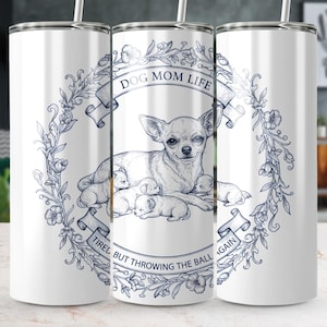 Puede incluir: Vaso blanco con una ilustración detallada de un chihuahua con cachorros, rodeado por una corona floral. El texto dice "DOG MOM LIFE" y "TIRED BUT THROWING THE BALL AGAIN" en una pancarta. Incluye una pajita.
