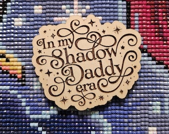 May include: A wooden sign with the text "In my shadow daddy era" in a decorative font. The sign is surrounded by small stars.