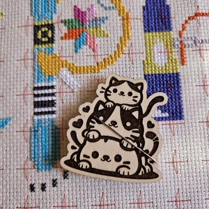 May include: Wooden cutout of three stacked cats with black and white markings. The cats are smiling and have hearts around them.