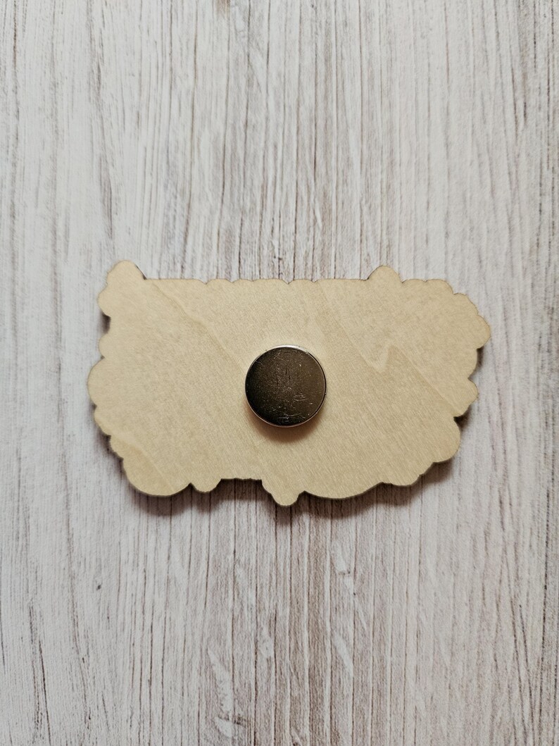 May include: A wooden cutout of a flower with a magnetic backing. The cutout is light brown and has a detailed design.
