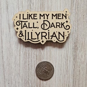 May include: A wooden sign with the text "I like my men: Tall, Dark & Illyrian." The sign is on a light wood background.