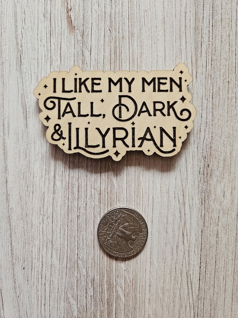 May include: A wooden sign with the text "I like my men: Tall, Dark & Illyrian." The sign is on a light wood background.