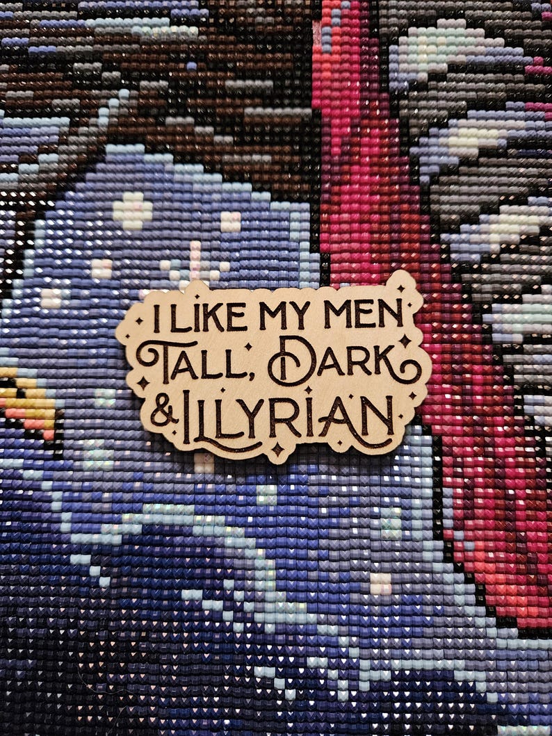 May include: A wooden sign with the text "I like my men tall, dark & Illyrian." The sign has a brown background and white lettering.