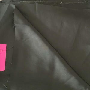 May include: Dark green satin poly lining fabric, 60" x 1 1/8 yd, is displayed. The fabric is folded and draped, showing its smooth texture. A pink sticky note with handwritten text is visible.