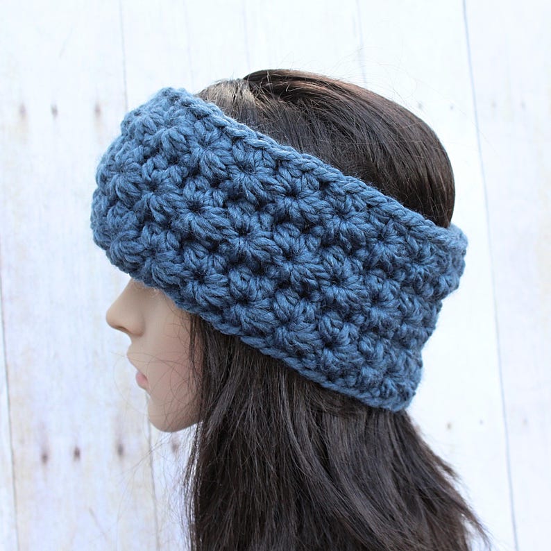May include: A blue crocheted headband with a textured stitch pattern. The headband is worn on a person with long dark hair.