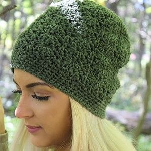 May include: A green crocheted beanie hat with a textured stitch pattern. The hat is worn by a person with long blonde hair.
