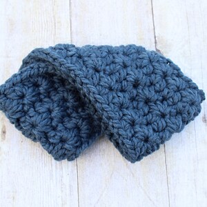 May include: A blue crocheted headband folded in half. The headband is made with a textured stitch.