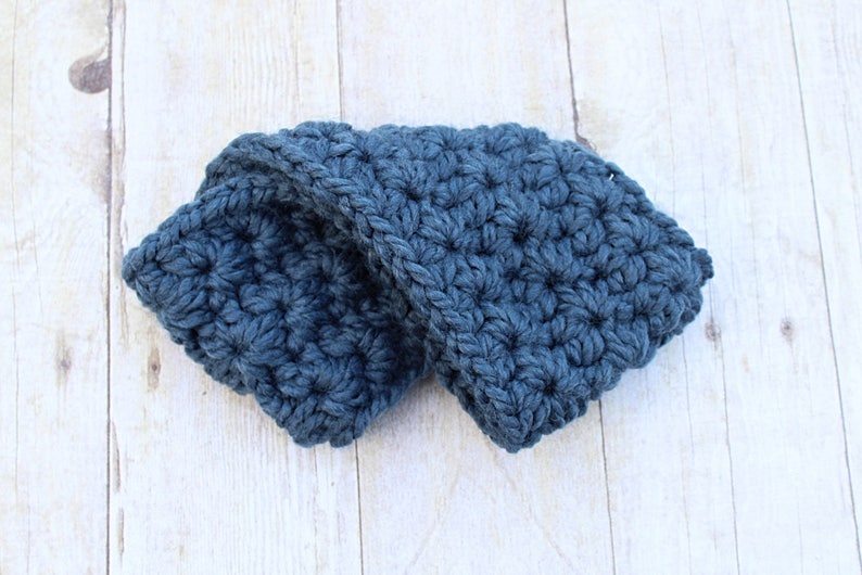 May include: A blue crocheted headband folded in half. The headband is made with a textured stitch.