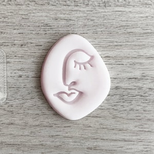 Może przedstawiać: Dwa silikonowe formy do rękodzieła, jedna przezroczysta, a druga różowa, obie z prostym rysunkiem liniowym twarzy z zamkniętym okiem, nosem i ustami.