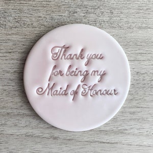 May include: A clear plastic stamp with the text "Thank you for being my Maid of Honour" and a pink ceramic coaster with the same text.
