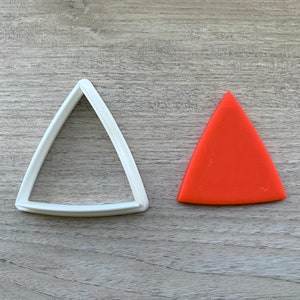 Könnte beinhalten: Ein weißer Plastik-Dreiecks-Ausstecher und ein durchgefärbter orangefarbener Dreiecks-Ausstecher.