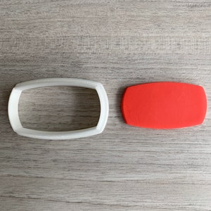 Puede incluir: Un cortador de galletas de plástico blanco con forma de rectángulo con bordes redondeados, junto a un cortador de galletas de plástico rojo con forma de rectángulo con bordes redondeados.