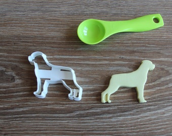 Könnte beinhalten: Zwei hundeartige Ausstecher, einer weiß und einer hellgrün, auf einer braunen Holzoberfläche. Ein grüner Messlöffel aus Plastik ist ebenfalls im Bild.