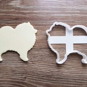 May include: A white plastic cookie cutter in the shape of a Pomeranian dog. The cutter is shown next to a solid white version of the cutter.