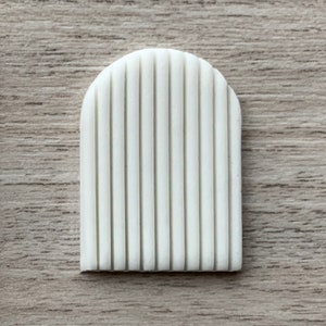 Könnte beinhalten: Weiße Silikonform mit einem erhabenen, gewölbten Design. Die Form hat eine Reihe von vertikalen Linien, die sich über die gesamte Länge des Bogens erstrecken.