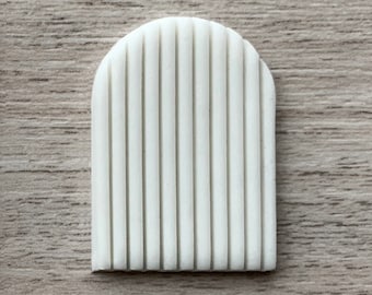Puede incluir: Molde de silicona blanco con un diseño arqueado elevado. El molde tiene una serie de líneas verticales que recorren la longitud del arco.