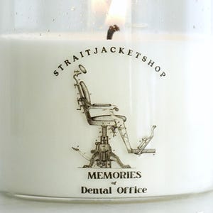 May include: A clear glass candle jar filled with white wax and a lit wick. The label features a black line drawing of a vintage dental chair, the text STRAITJACKETSHOP, and the words MEMORIES of Dental Office. A round bamboo lid sits nearby.