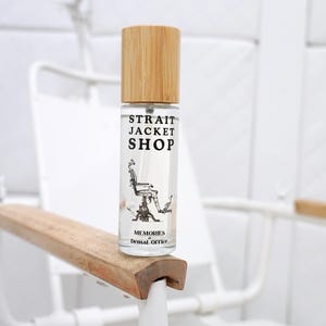 May include: A clear glass spray bottle with a light wood cap. The label features the text "STRAIT JACKET SHOP" above a black and white illustration of a dental chair, with the text "MEMORIES of Dental Office" printed below the illustration.