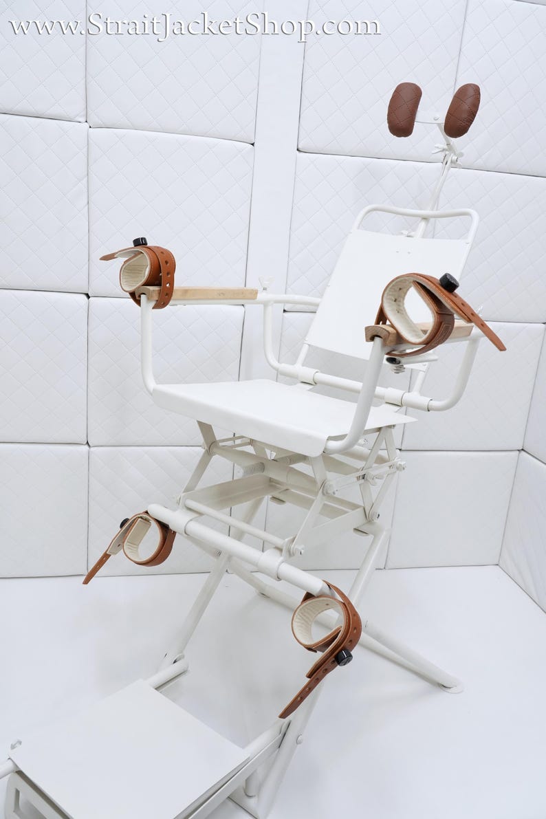 May include: White metal restraint chair with brown leather straps and headrests. The chair has a footrest and adjustable height.