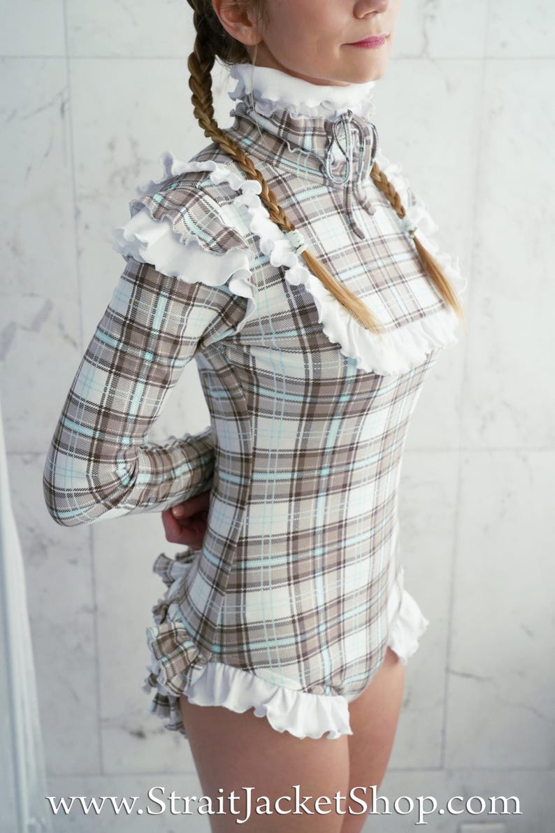 May include: A long-sleeved plaid bodysuit in shades of brown, white, and light blue, trimmed with white ruffles. The garment has a high collar and a zipper closure. The website address www.StraitJacketShop.com is visible at the bottom.