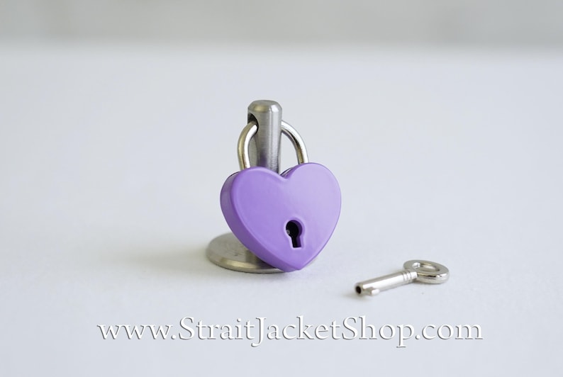 May include: A small purple heart-shaped padlock with a silver key. The padlock is on a silver stand.